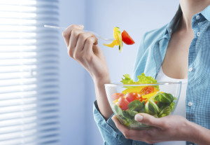 Woman holding a bowl and eating salad in front of a window.