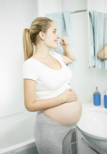 beautiful pregnant woman brushing teeth at bathroom